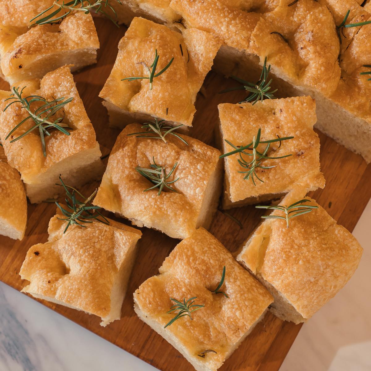 Focaccia com alecrim cortada em quadrados sobre tábua de madeira