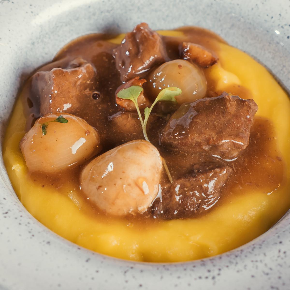 Cubos de carne ao molho com cebolas pérola sobre purê amarelo