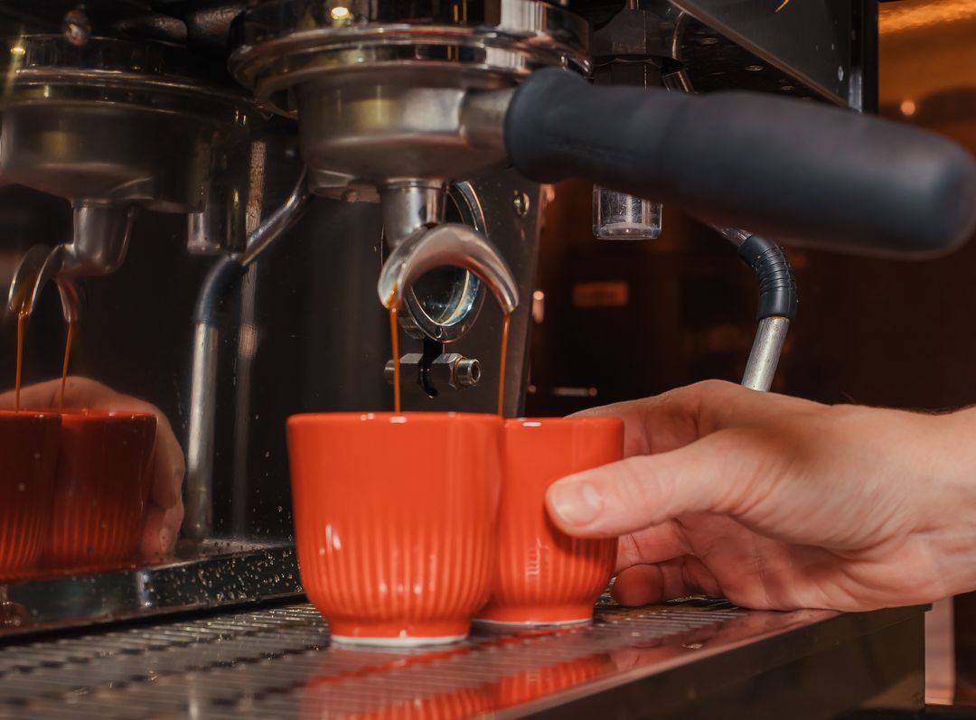 Máquina de espresso servindo dois cafés em xícaras laranja